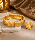 A gold-plated traditional Indian bracelet and matching ring set displayed on a marble block with a gold lantern and satin fabric in the background.
